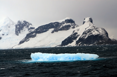 Surreal looking image of a blue iceberg in a somewhat dramatic Antarctic background