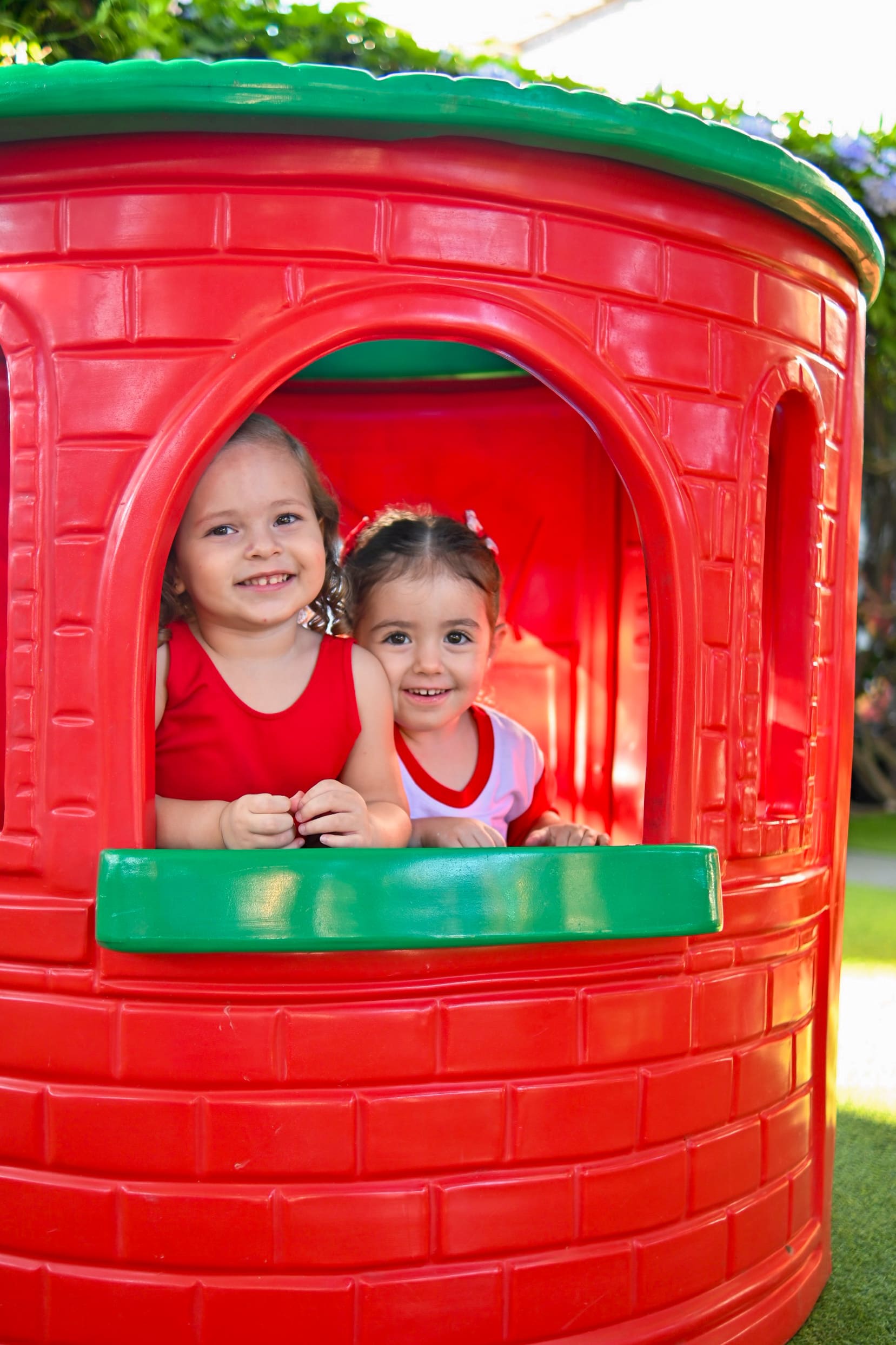 Duas crianças do Toque de Mãe sorrindo na janela da casinha do playground