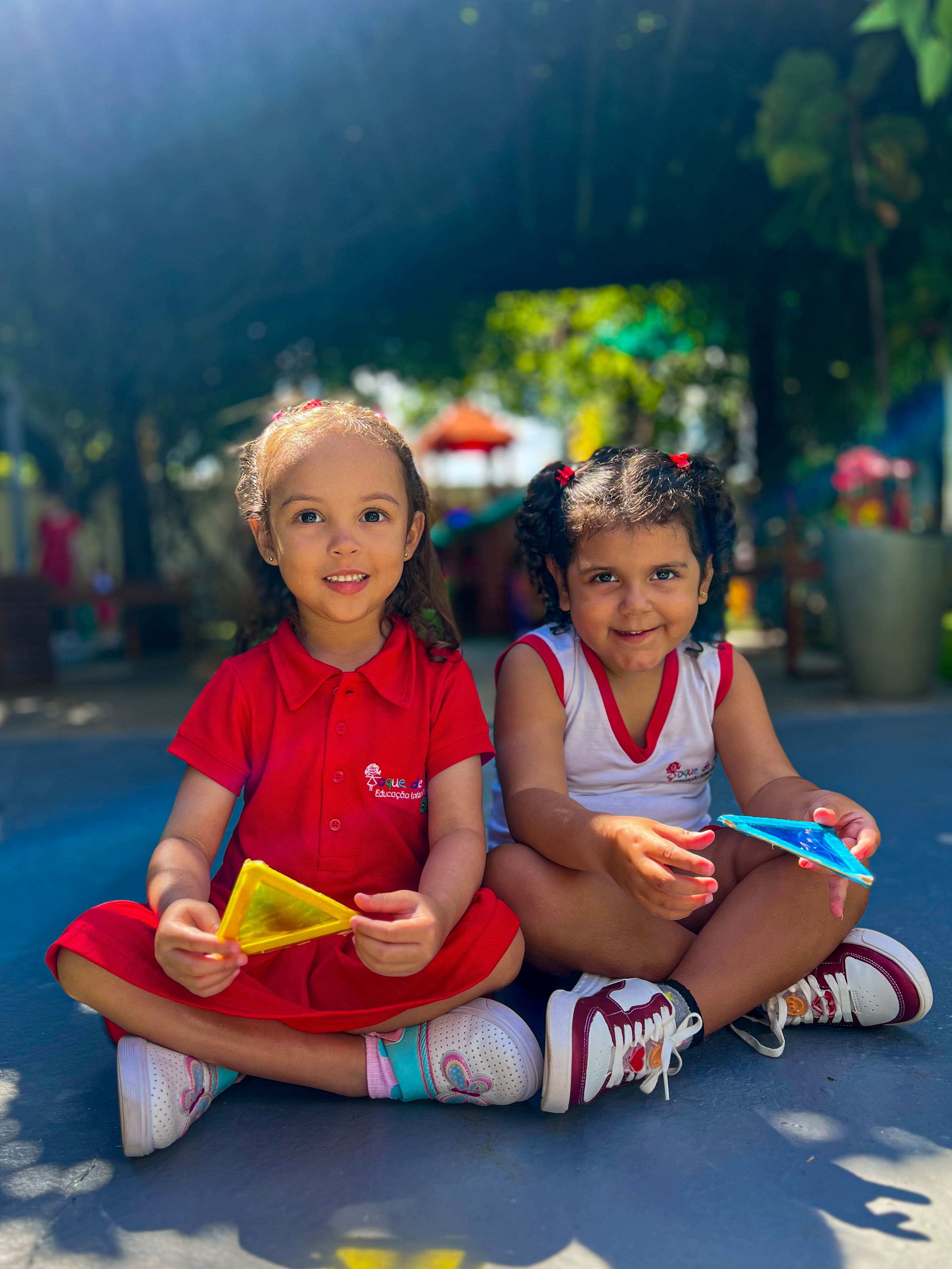 Duas crianças sentadas no chão brincando com peças coloridas, à sombra