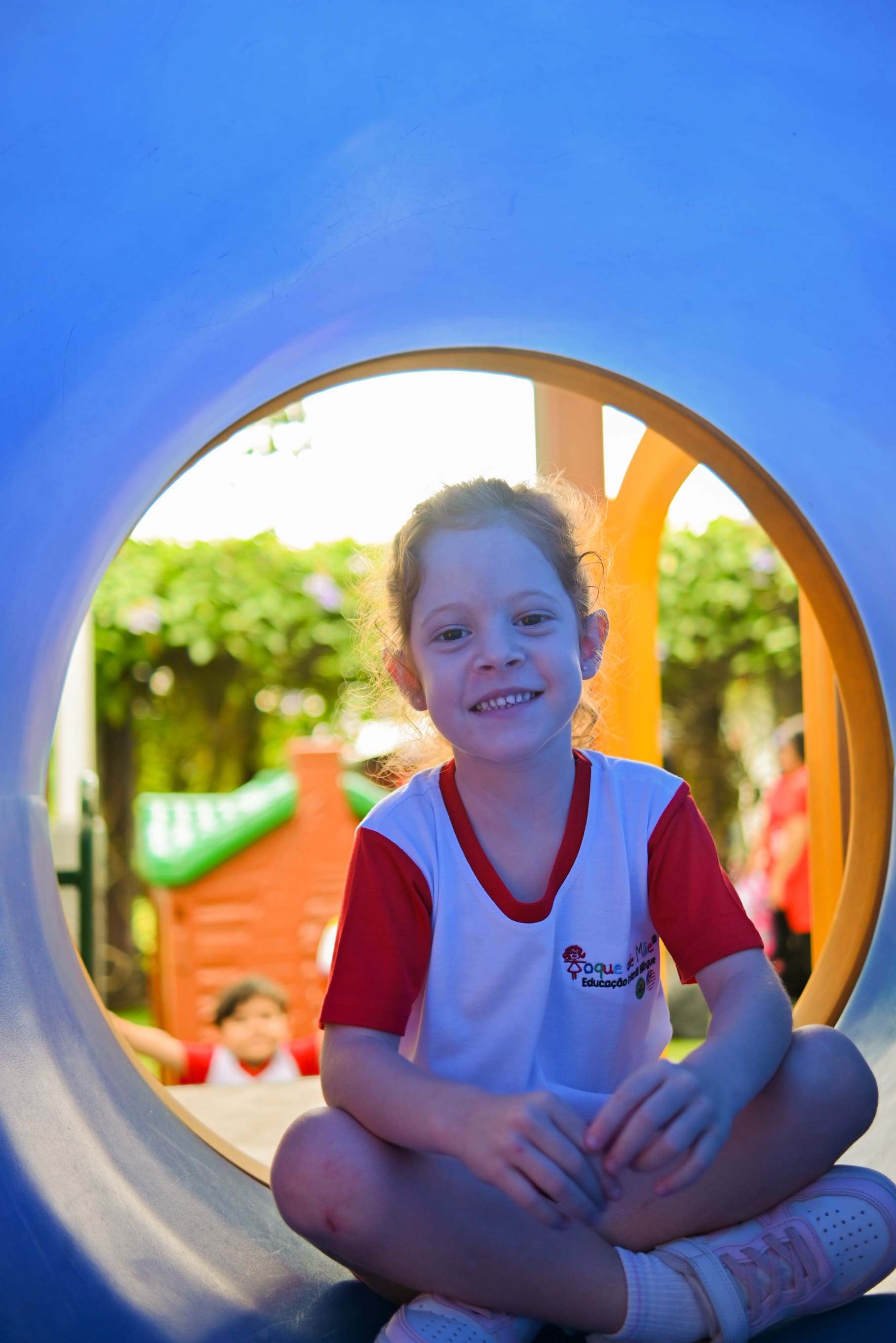Menina sentada dentro do túnel do playground, sorrindo para a câmera