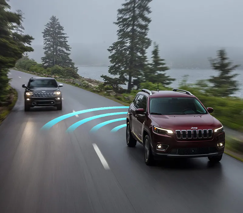The 2021 Jeep Cherokee illustrated with sensors monitoring the rear side blind spot area as it detects a vehicle coming up behind it in the next lane