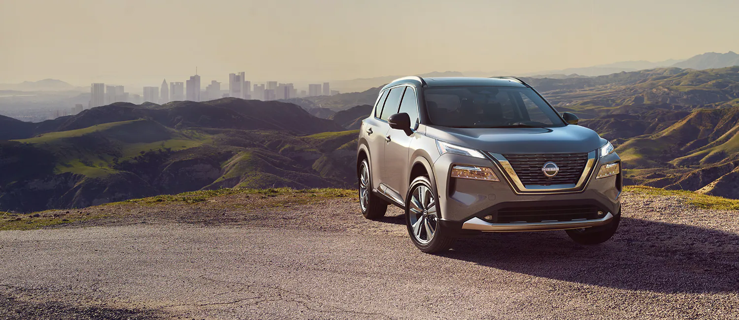 2022 Nissan Rogue on hilltop with city in background.