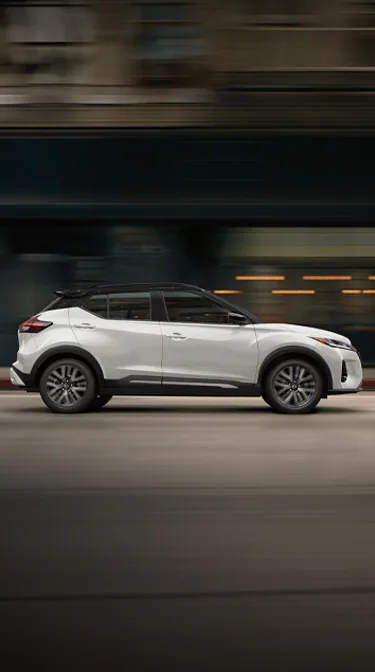 2024 Nissan Kicks in white, profile driving on a downtown street