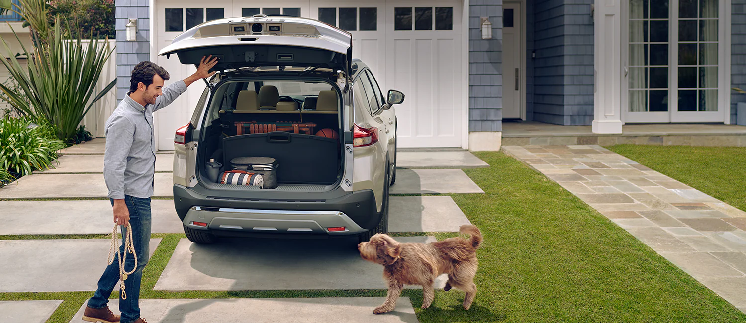 2024 Nissan Rogue with hatch open, a man with a leash and a dog illustrating cargo capacity.
