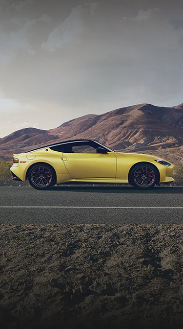 2024 Nissan Z in yellow driving on a desert road with mountains in the distance