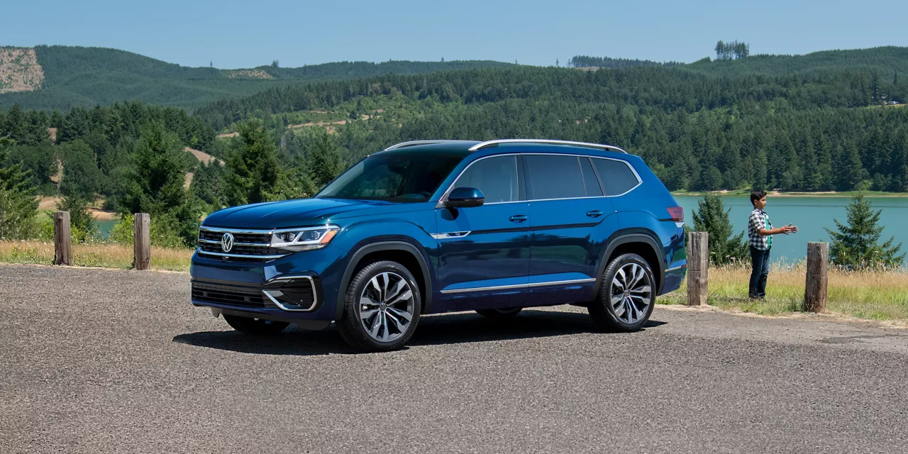 Atlas shown in Tourmaline Blue Metallic parked with people in foreground and a lake and forest in background.