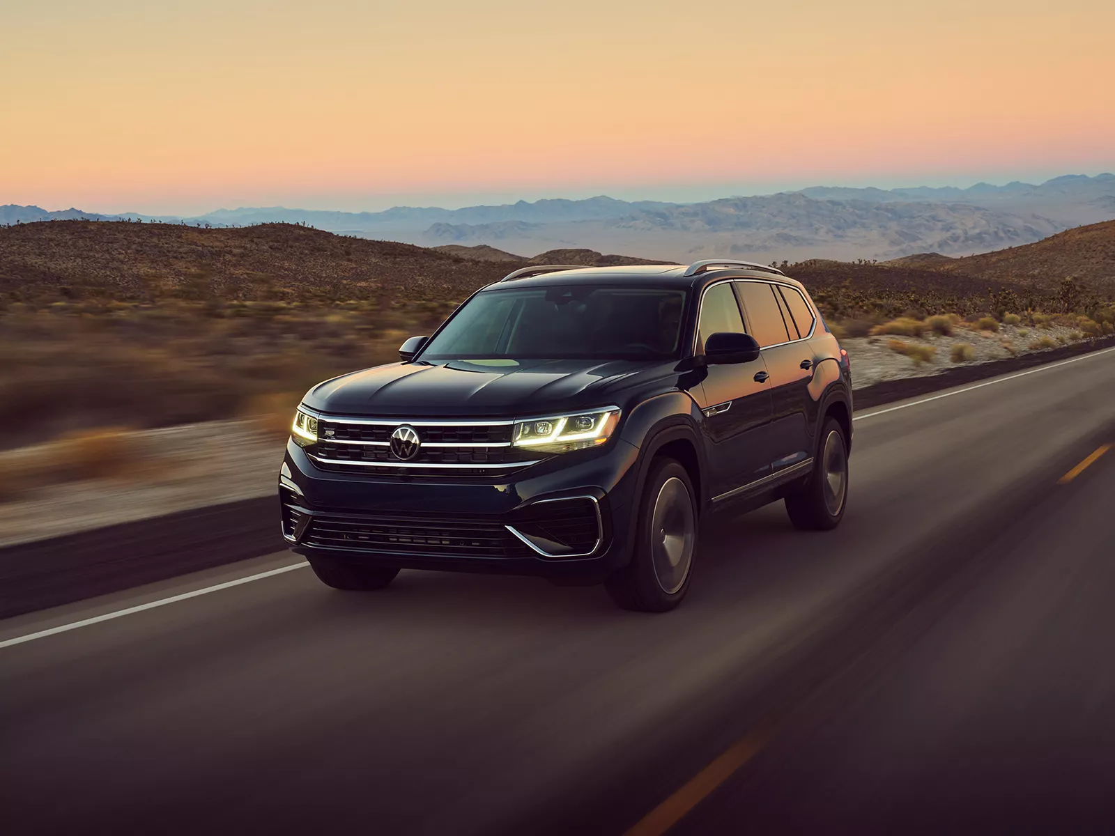 An Atlas shown in Blue Metallic, driving on a two-lane road with mountains in background, as seen from the driver side.