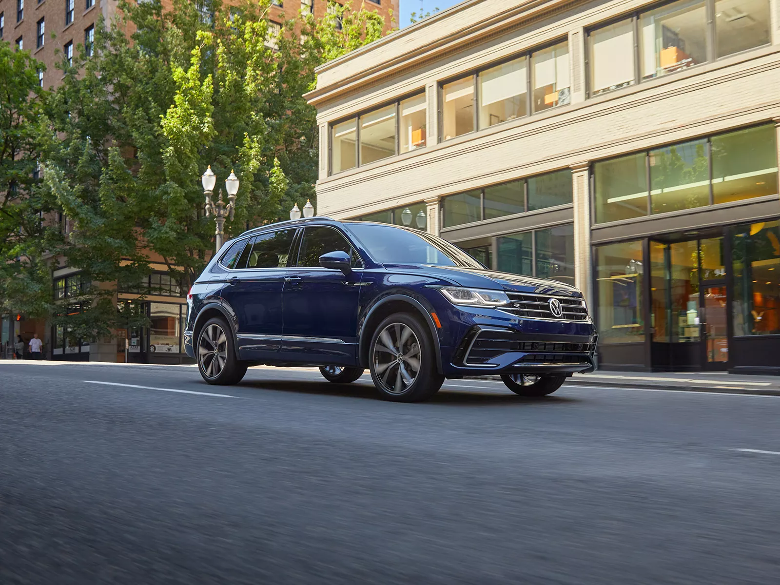 A Tiguan shown in Atlantic Blue Metallic drives through a modern, downtown area.