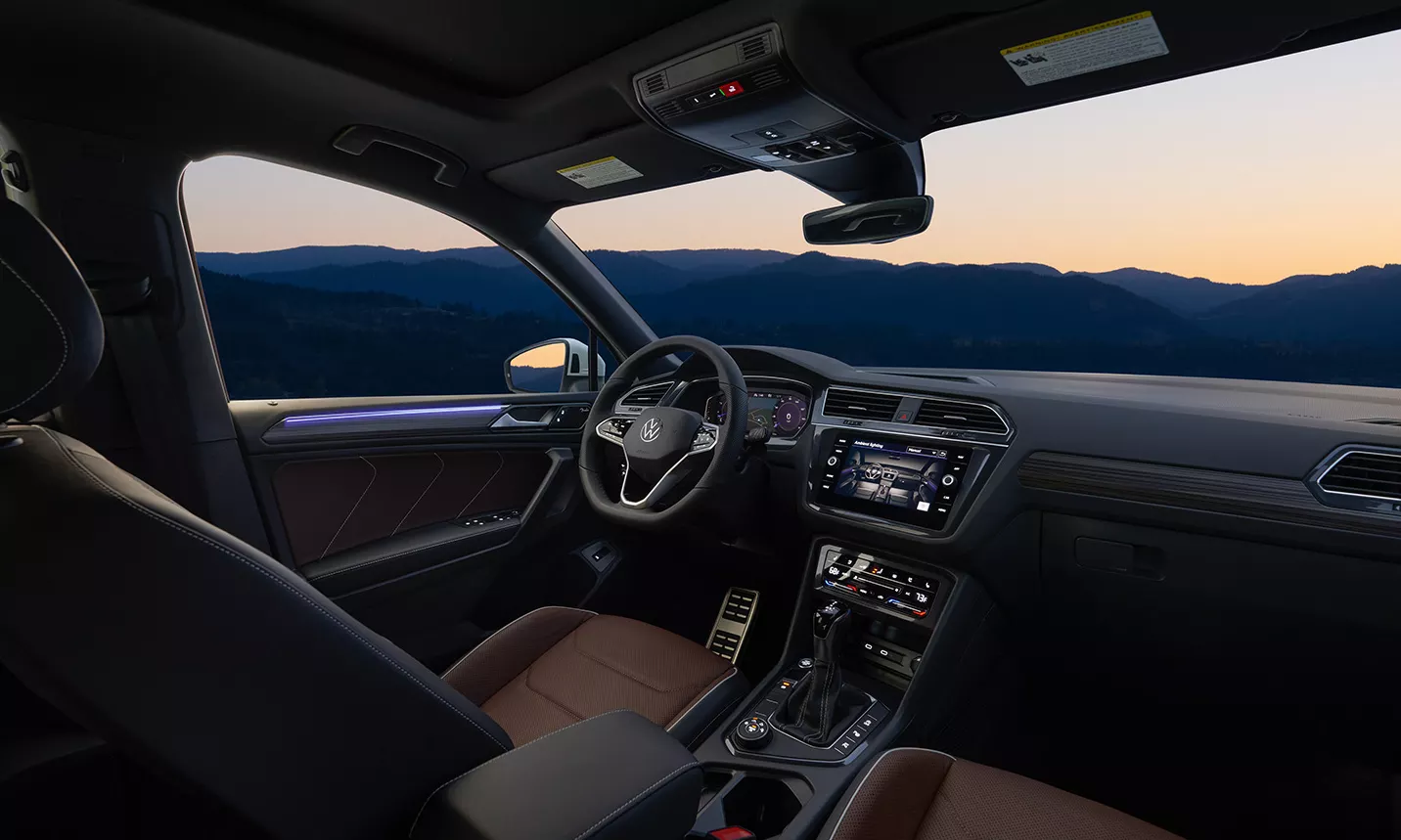 Interior view from passenger seat of Tiguan driver’s area, showing displays, steering wheel, and ambient lighting around trim and dash.