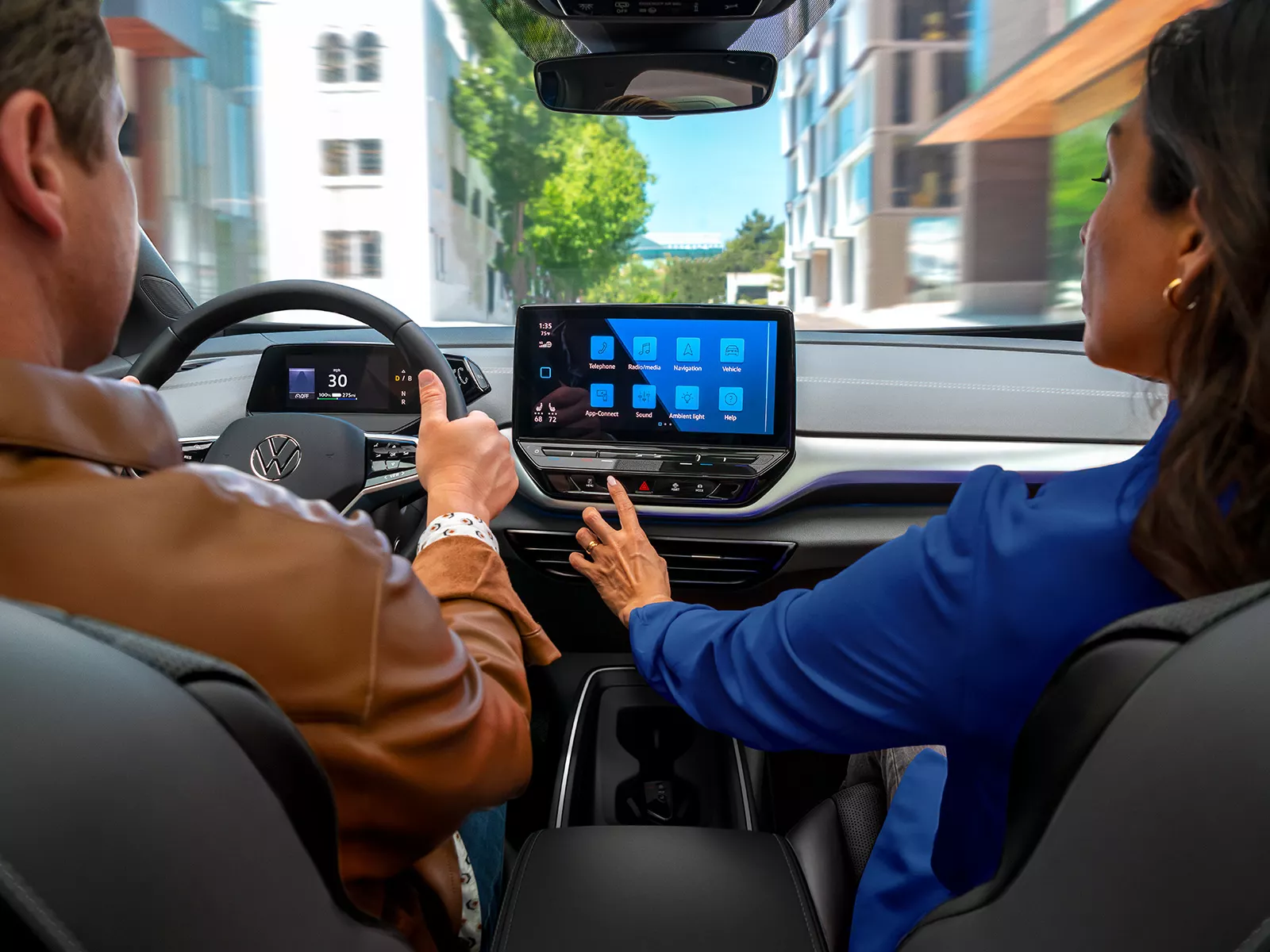 A close-up, over the shoulder shot of an ID.4 dashboard, focusing on the center display as the passenger reaches out to the touchscreen.