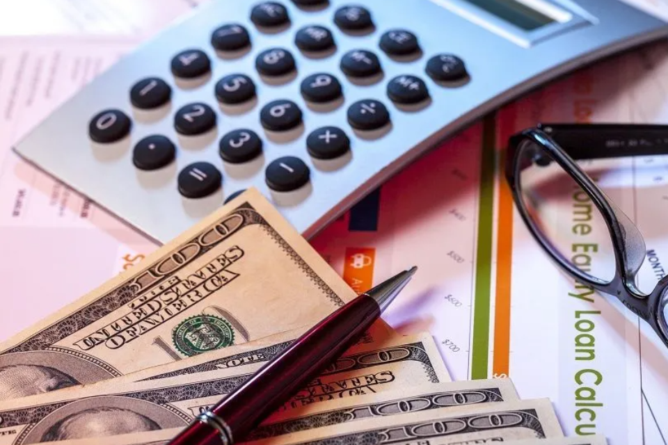 A photo that shows cash, a pen, a calculator, a pair of glasses and a paper that says home equity loan calculator
