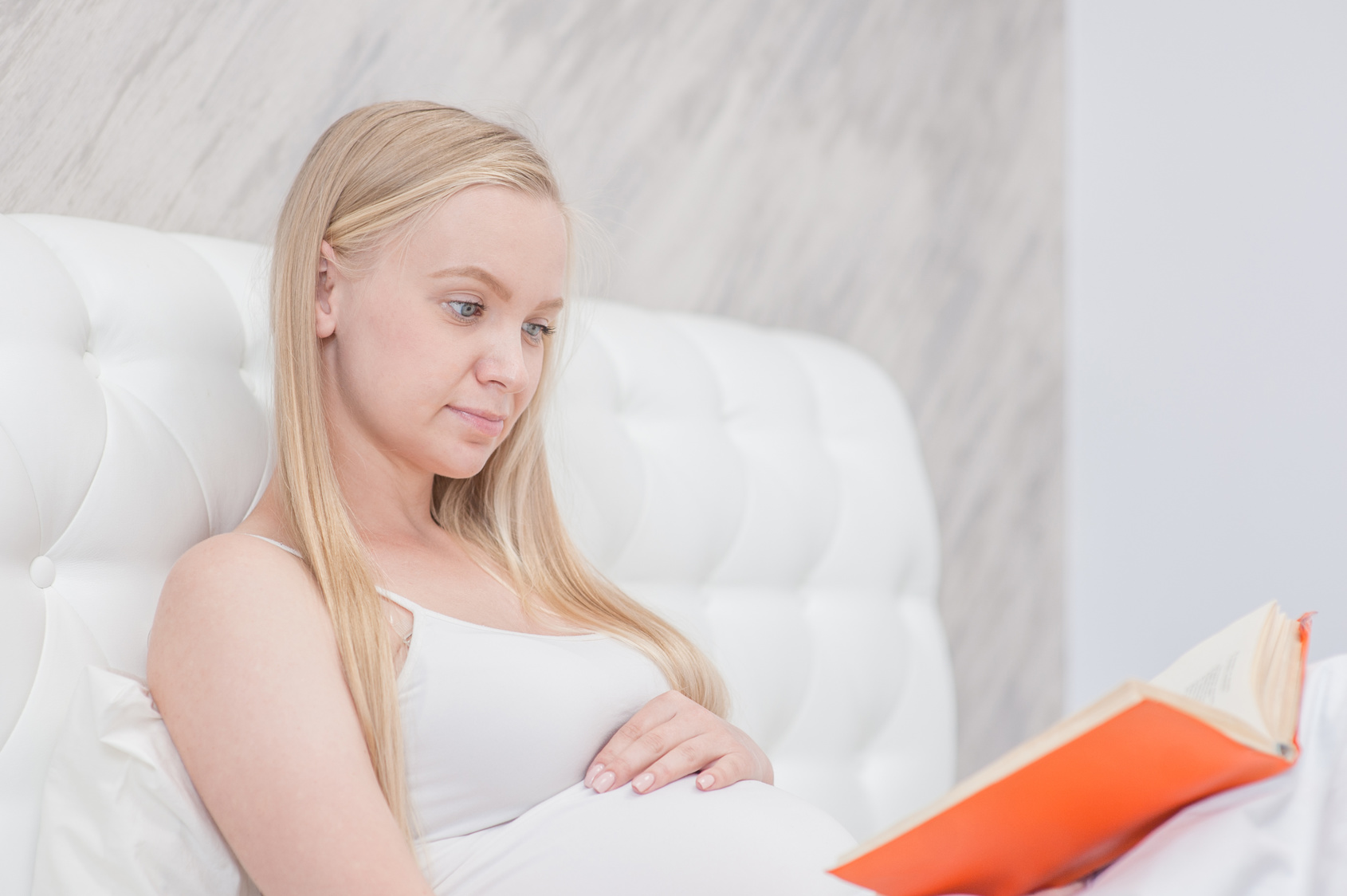 Pregnant woman reading book in his bed at home. Empty space for text