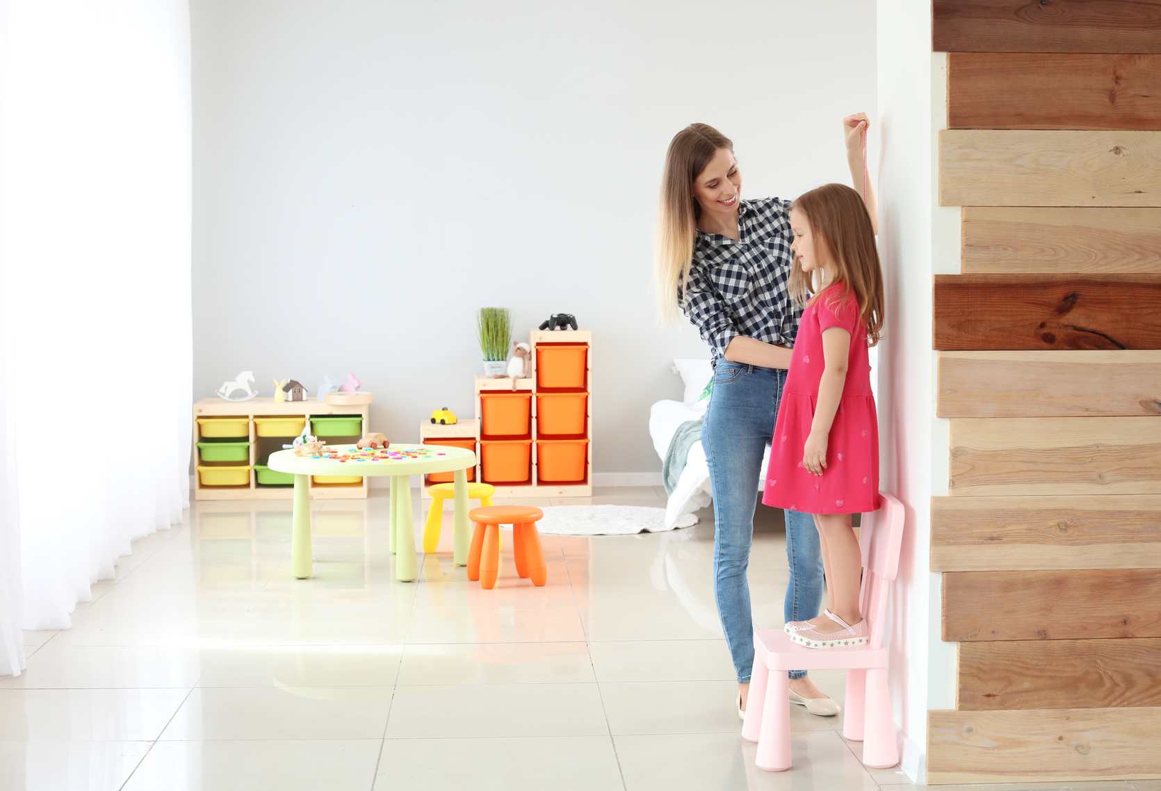 Young mother measuring height of her little daughter at home