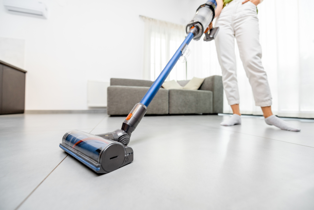 Woman cleaning floor with cordless vacuum cleaner in the modern white living room. Concept of easy cleaning with a wireless vacuum cleaner