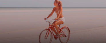 Foto de uma mulher pedalando em uma bicicleta em uma praia. Ela representa um colaborador em férias e as regras para as férias.
