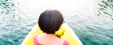 Mulher sentada em um barco sobre a água espelhada, representando um momento de férias.