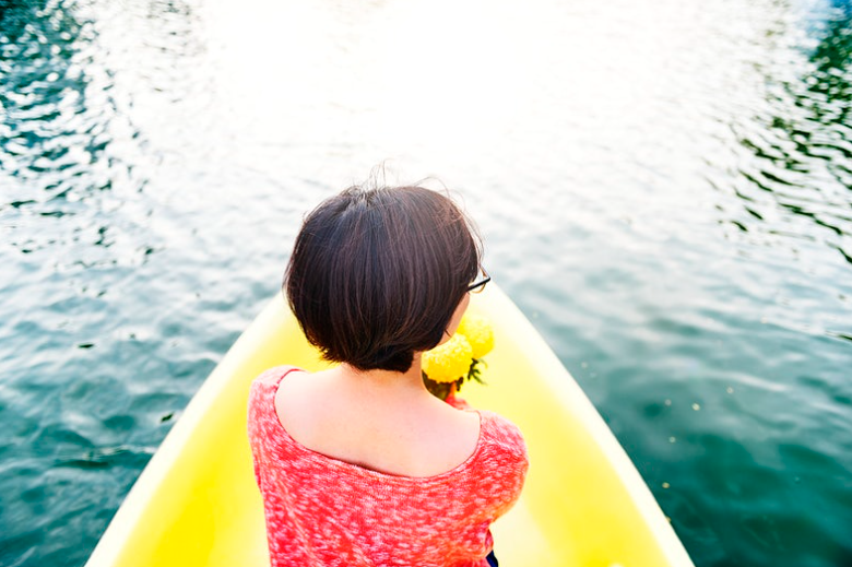 Mulher sentada em um barco sobre a água espelhada, representando um momento de férias.