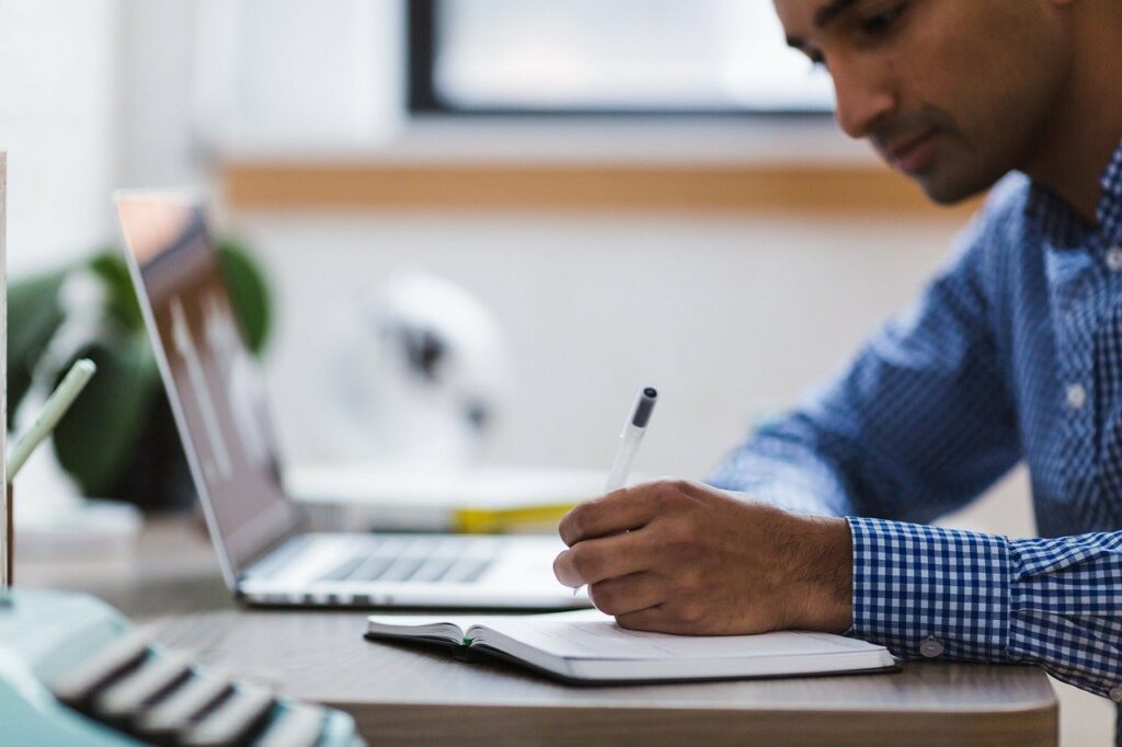 Imagem retrata um home com um bloco de notas, uma caneta e um notebook retratando as dificuldades da liderança no home office