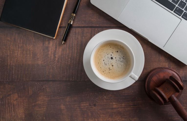 foto de uma mesa de juiz com martelo, café e computador, representando o julgamento das condições de trabalho de uma empresa