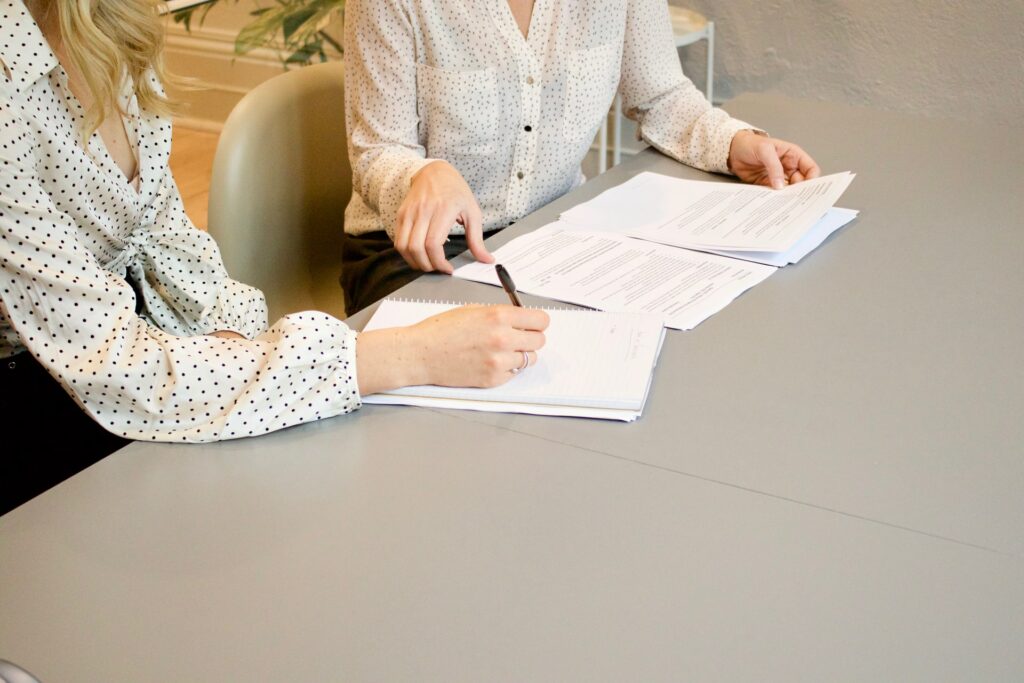 Duas mulheres sentadas à uma mesa, assinando os papéis da demissão