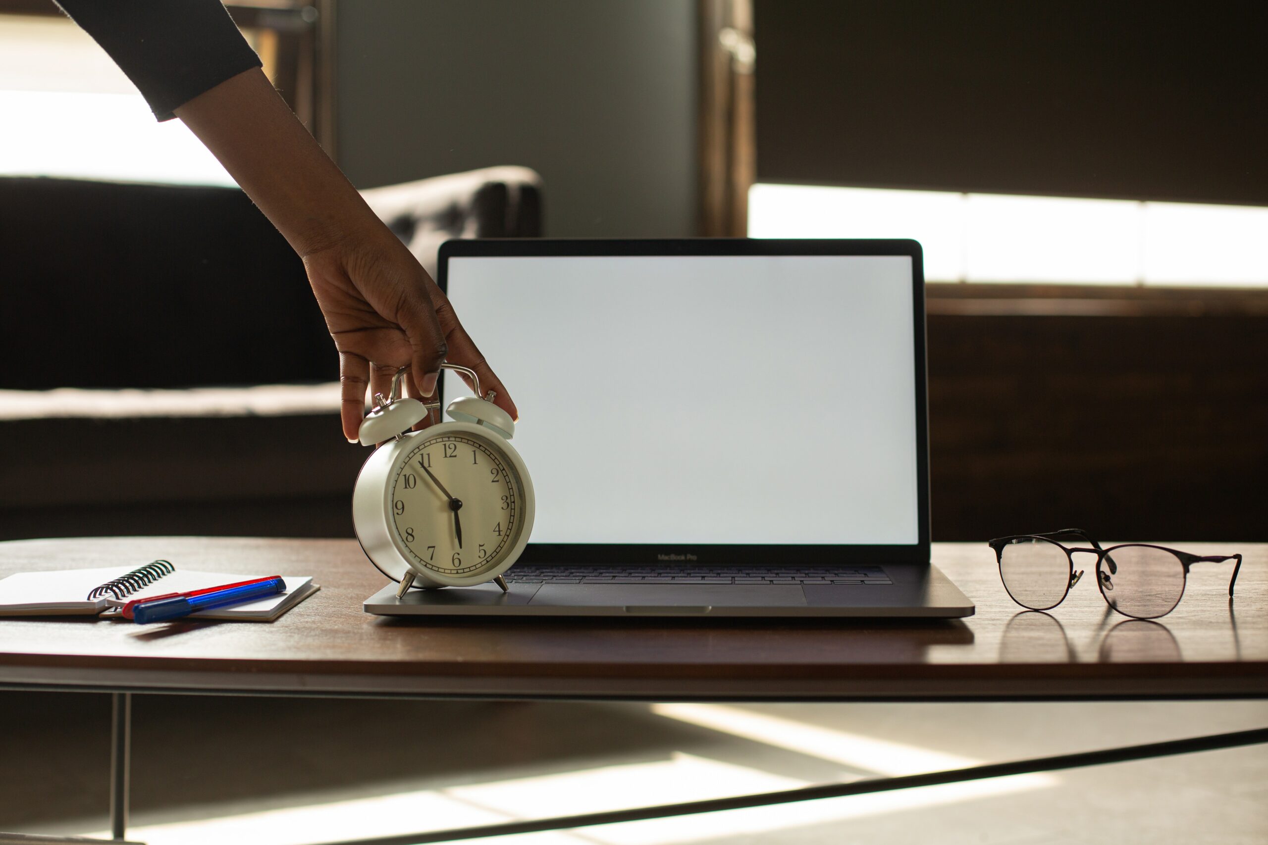 Mão segurando um relógio enfrente a um notebook em ambiente de trabalho, representando o calculo da DSR sobre horas extras.