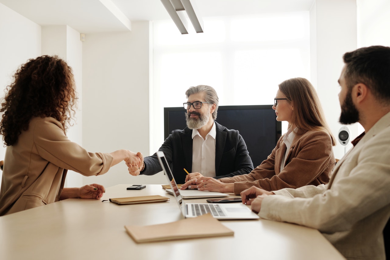 Quatro pessoas sentadas ao redor de uma mesa em um ambiente de entrevista de emprego, sendo dois homens e duas mulheres.