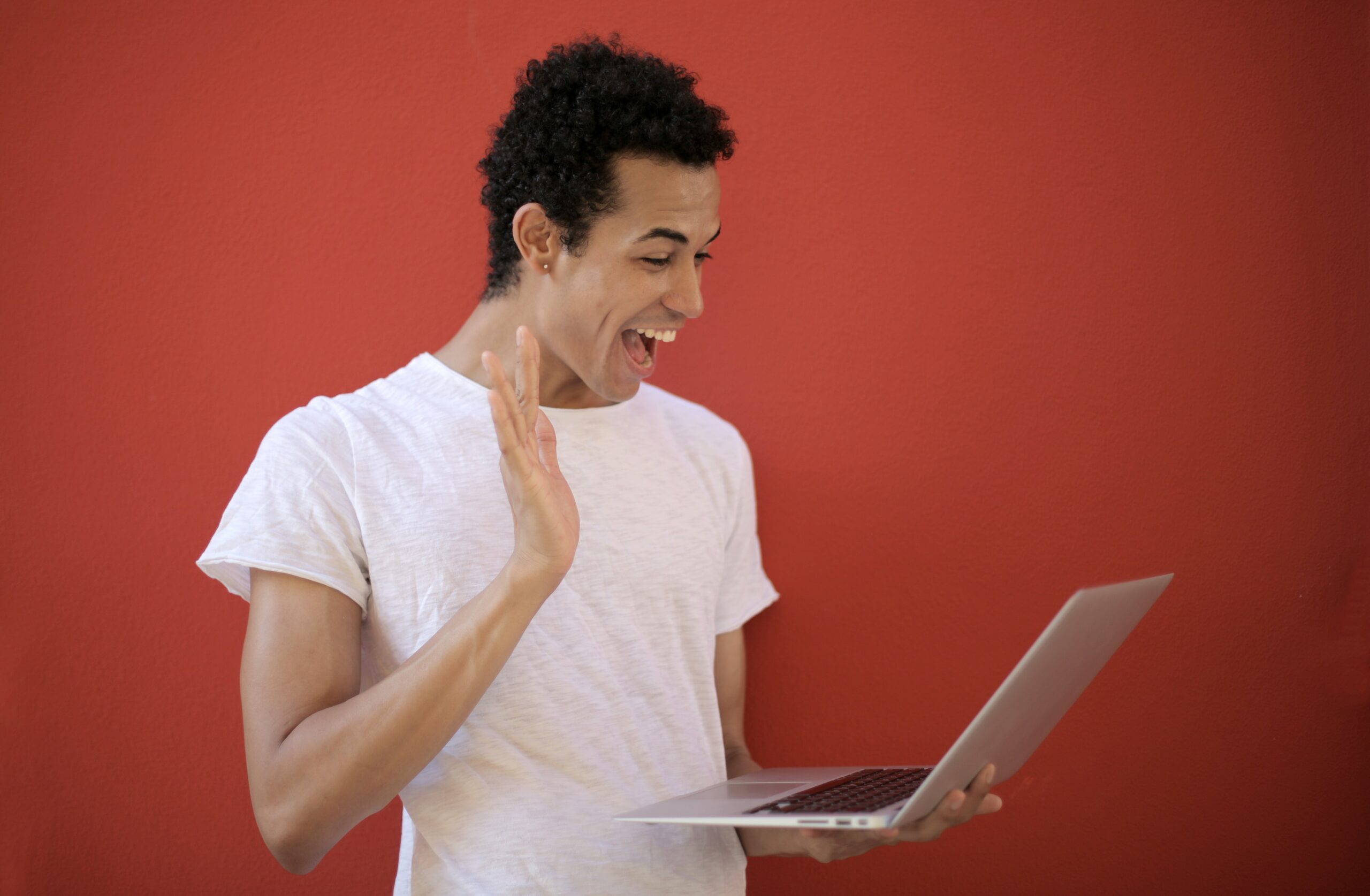 Um homem sorri e acena para a tela do notebook que está segurando com a outra mão.