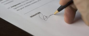 assinatura de contrato, mão apoiando sob o papel com uma caneta, assinando documento.