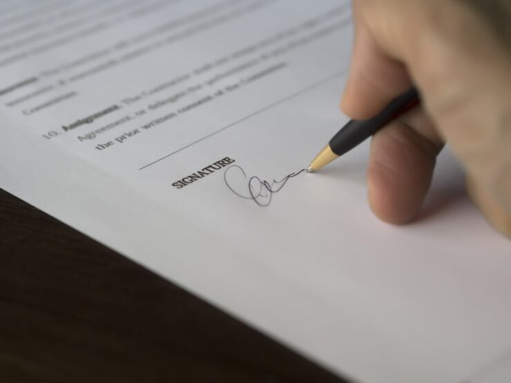 assinatura de contrato, mão apoiando sob o papel com uma caneta, assinando documento.