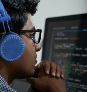 Homem de fone olhando para a tela de um computador que apresenta gráficos.