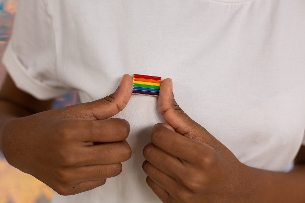 imagem com uma pessoa com a bandeira lgbt em um brochê pendurado na blusa