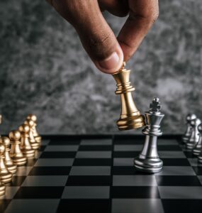 tabuleiro de xadrez com uma mão vindo pro cima, segurando uma das peças e realizando uma jogada.