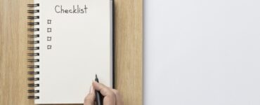 Mão escrevendo com um lápis em um caderno onde está desenhado um check list.