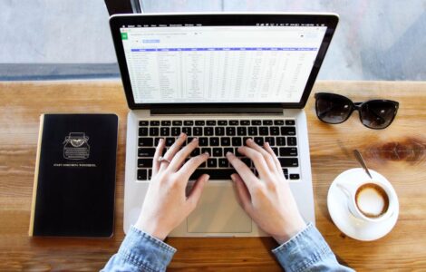 Mulher com café em sua mesa, utilizando computador e visualizando planilha de controle de férias