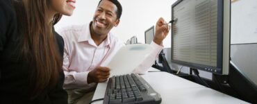 Homem negro mostrando banco de horas para servidor publico em computador para mulher que usa o computador
