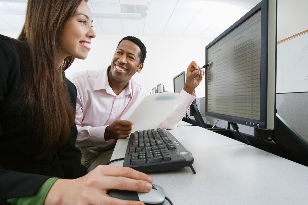 Homem negro mostrando banco de horas para servidor publico em computador para mulher que usa o computador