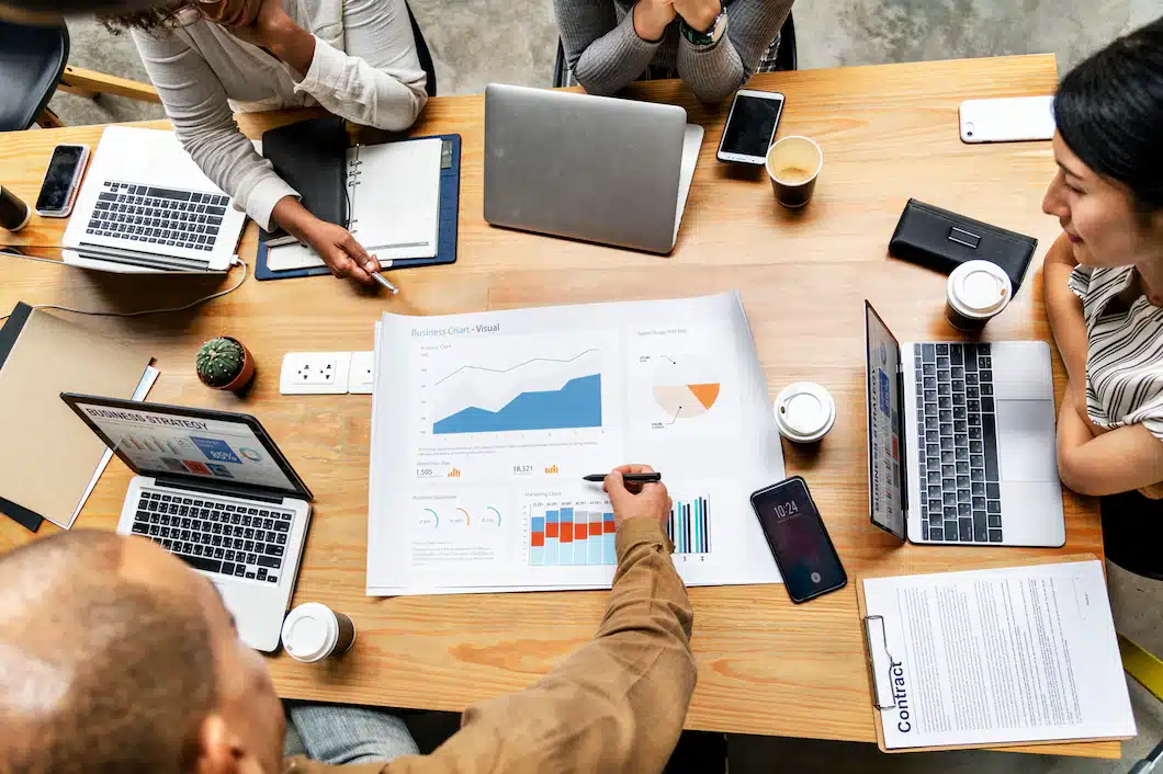 Homem mexendo em gráficos impressos sob uma mesa, ele está realizando Gestão Empresarial.