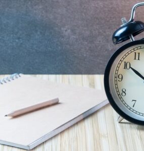 Relógio analógico ao lado de uma folha de papel e lápis para realizar a gestão de tempo no trabalho