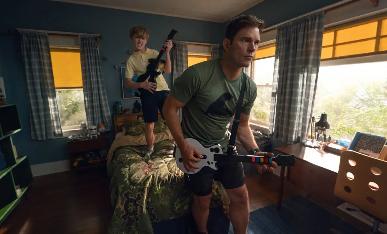 Chris Pratt e um garoto tocando guitarras de videogame em um quarto, cena do filme Way of the Warrior Kid