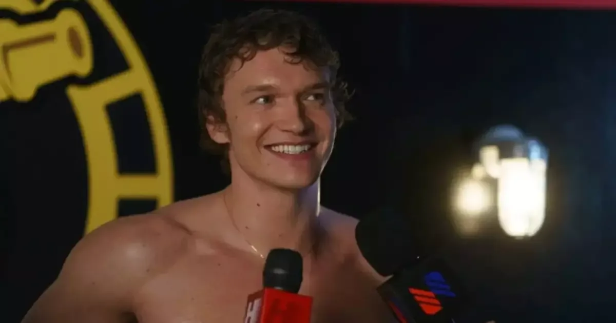 Connor Storrie sorrindo, sem camisa e com microfones à frente, em cena da série Rivalidade Ardente