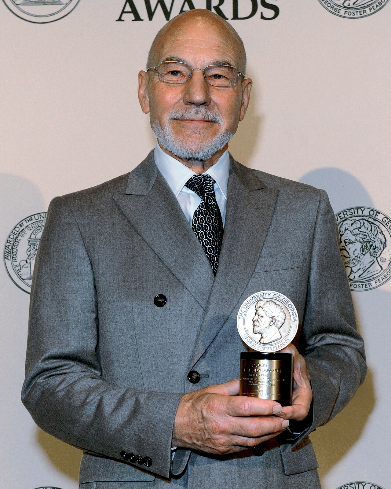 Patrick Stewart segura o troféu do Peabody Award de 2009, de terno cinza, em retrato de Wikimedia Commons