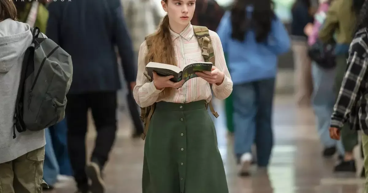 Carrie White caminha por um corredor lotado com um livro nas mãos, em imagem de divulgação da série