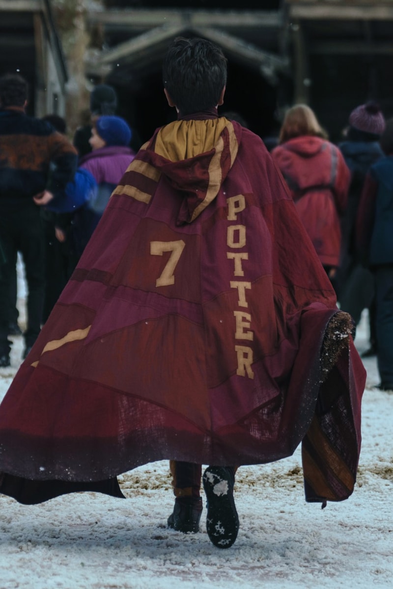 Harry de costas, com a capa do Grifinória com o número 7 e o nome Potter, caminhando na neve