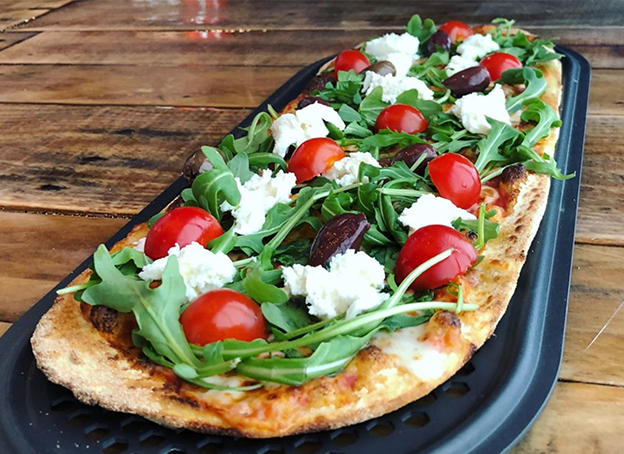 Close up of a pizza, topped with cheese, greens, and tomatoes