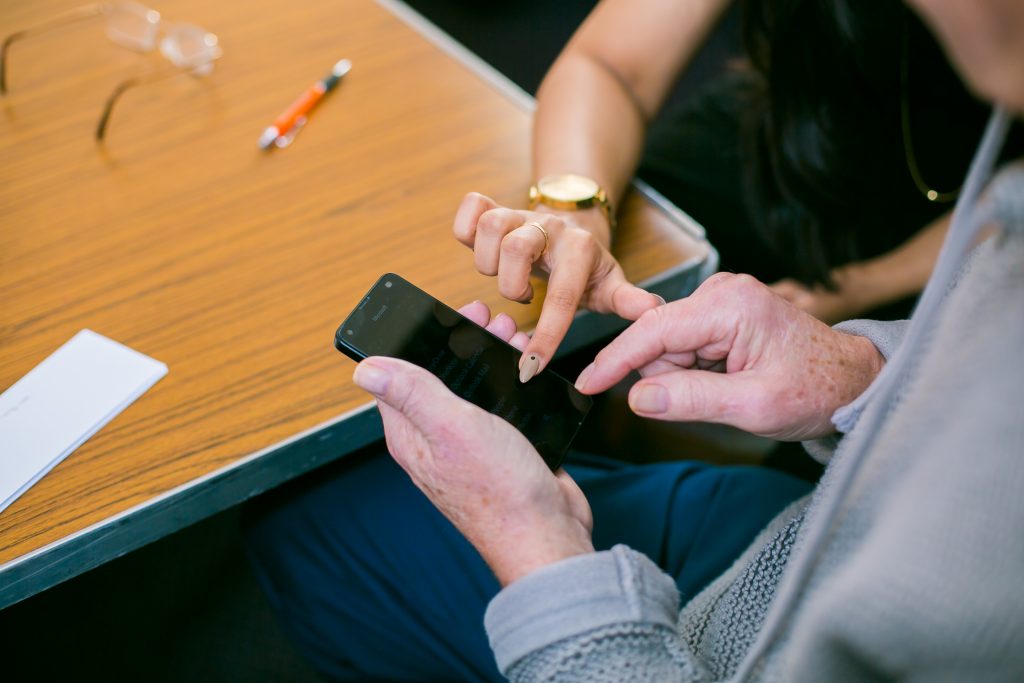 Photo of person holding a mobile phone with a Digital Champion showing how to use the touch screen.