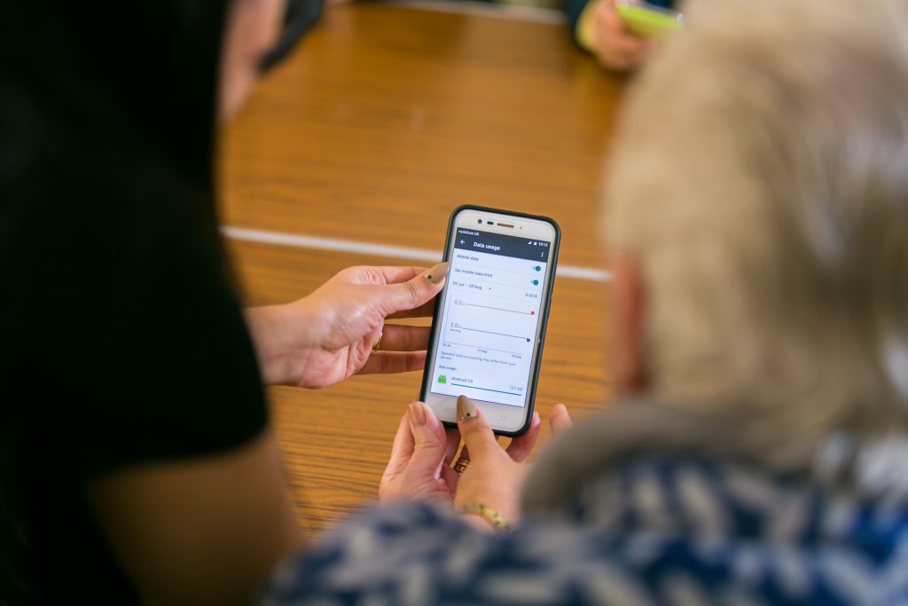 Photo of two people holding a mobile phoe, looking at the data usage data on the screen.