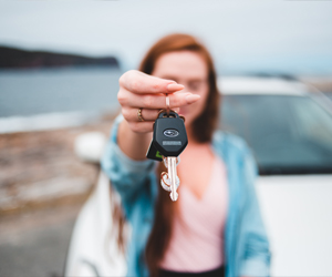 ein verschwommenes Hintergrundbild einer Frau, die einen Autoschlüssel nach vorne hält