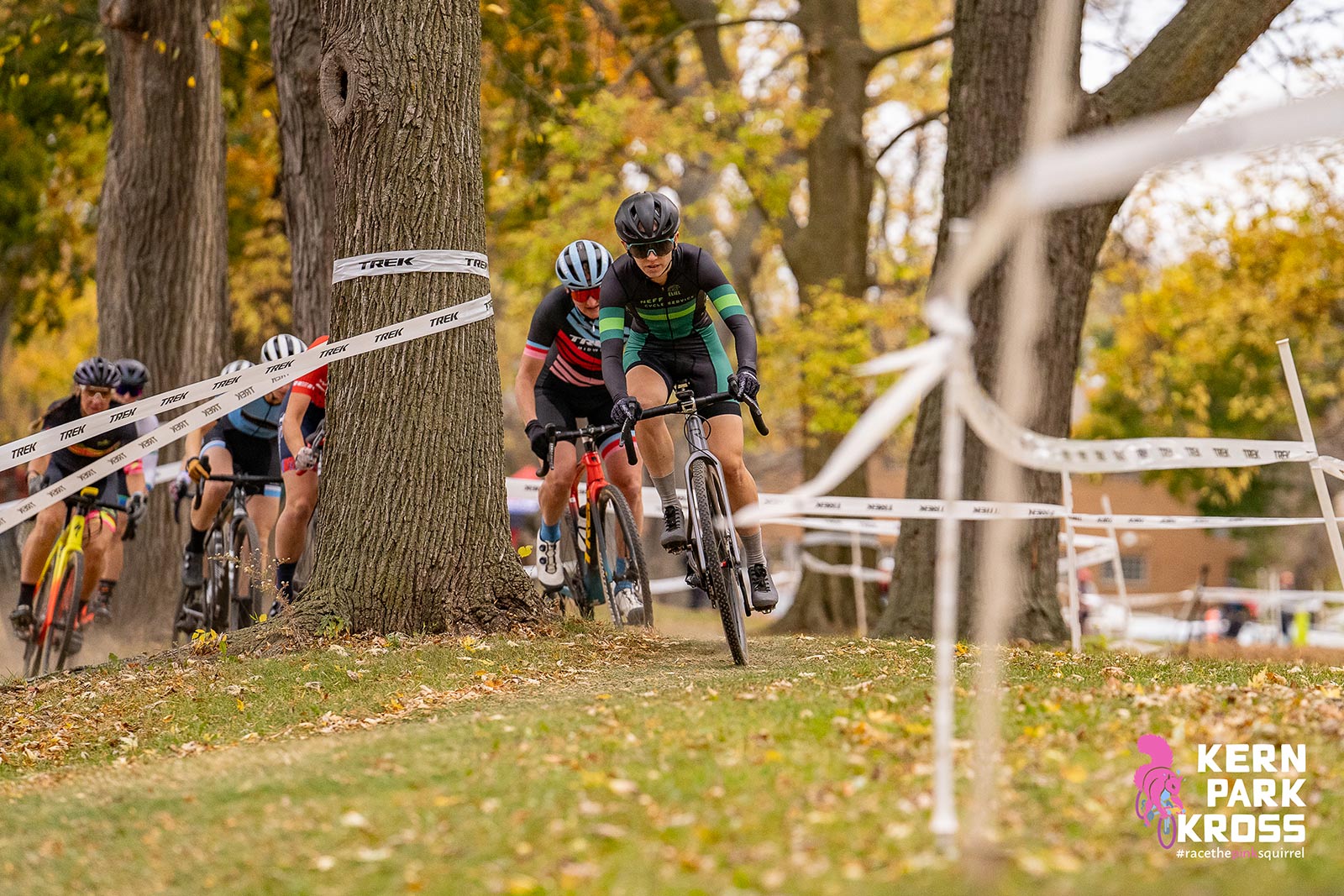 Several women navigating swiftly around a tree at a cyclocross race.