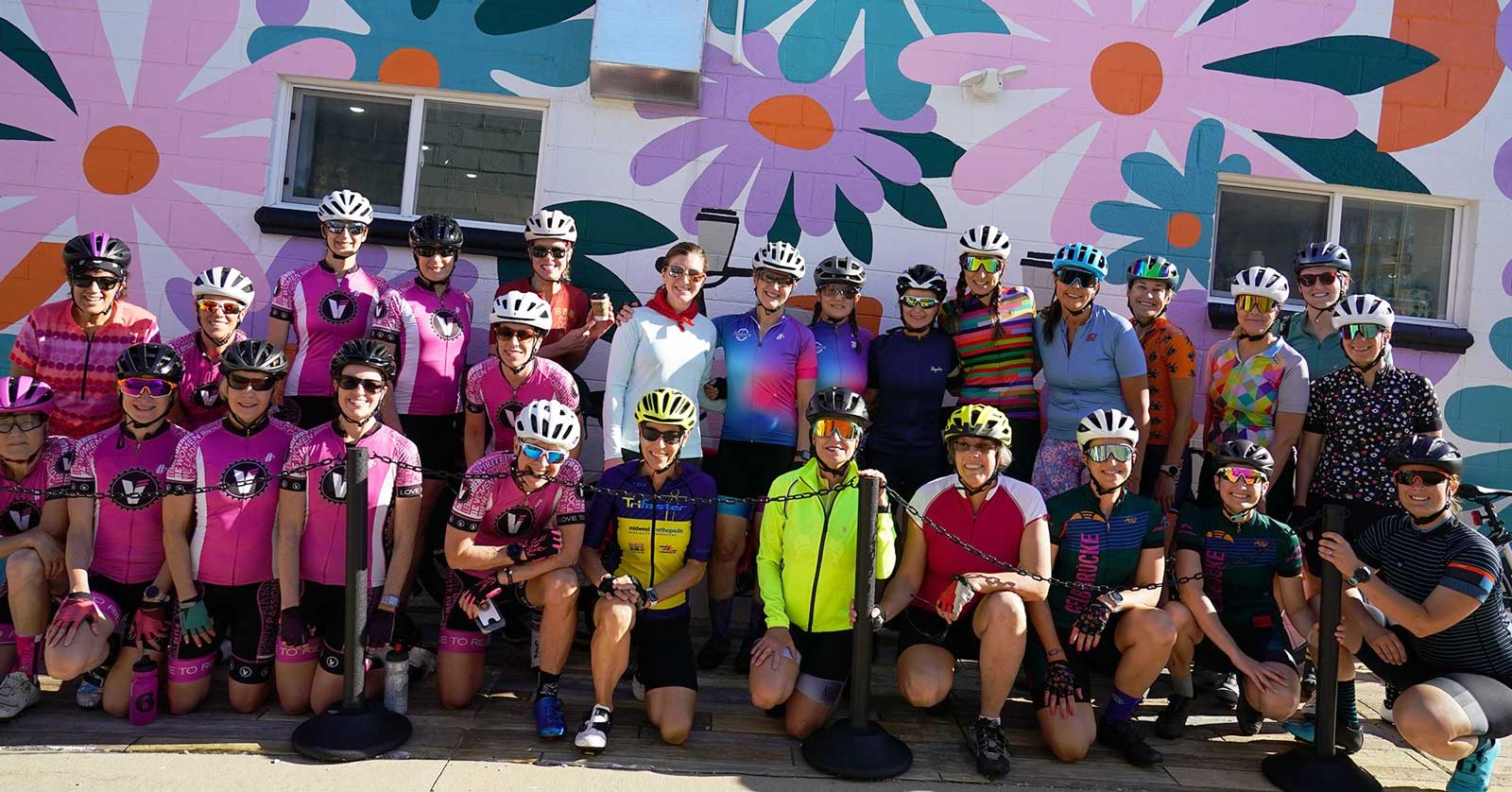 Doezens of women in cycling gear standing in front of a mural