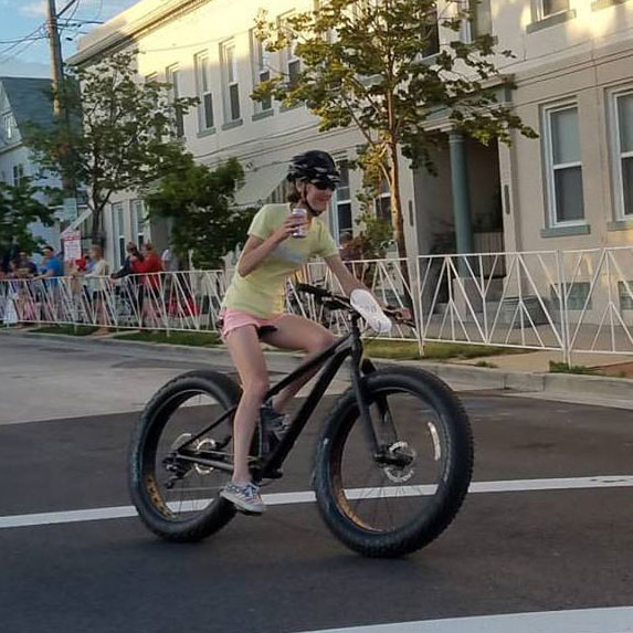 A woman holding a beer racing on a fat tire bike. Photo by Jason McDowell.